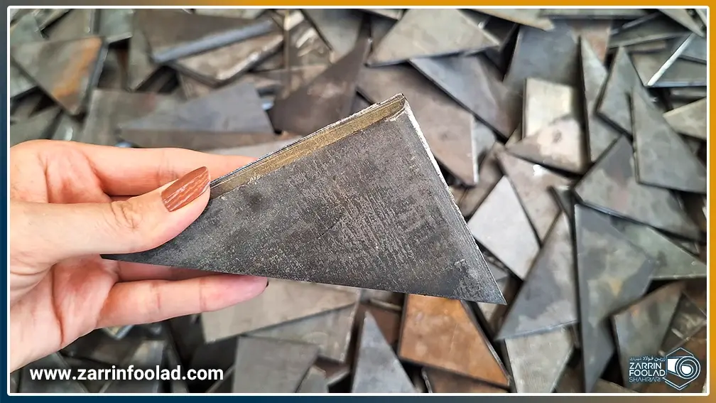 اپراتور، لچکی فولادی برش‌خورده‌ای را برای بررسی در دست دارد و در کنار دپوی لچکی‌های آهنی تولیدشده ایستاده است.